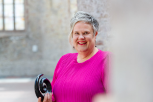 Deborah Jorritsma portrait in an old church smiling at the camera with a New Zealand koru in her hand.